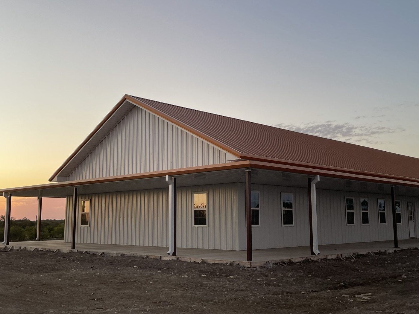 Custom cream barndominium with standing seam metal roof at sunset