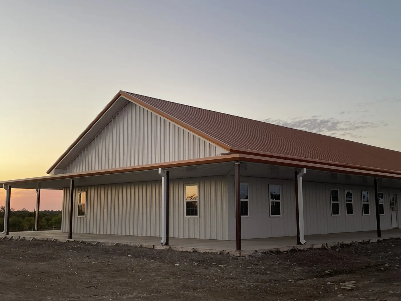 Custom cream barndominium with standing seam metal roof at sunset
